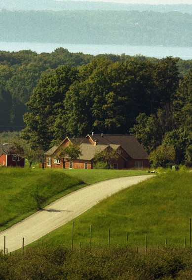 Large red brick home with plenty of green land and trees in the background and a lake in the distance