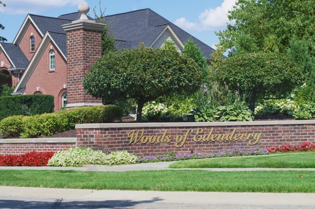 The front entrance of a neighborhood in Northville with a sign in front of a large brick home that says The Woods of Edenderry